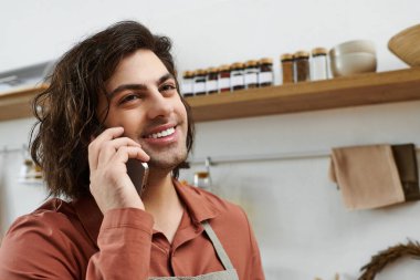 Neşeli genç adam, çağdaş mutfağında telefonla konuşurken gülümsüyor..