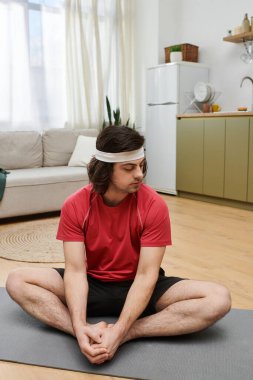 Formda genç adam evde yoga yapıyor, sağlık ve günlük egzersiz alışkanlıklarını destekliyor..