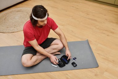 Genç bir adam yoga minderinde oturmuş diyabet malzemelerini inceliyor..