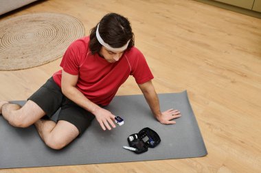 Genç bir adam, şık dairesinde yoga minderinde otururken kan şekerini ölçüyor..