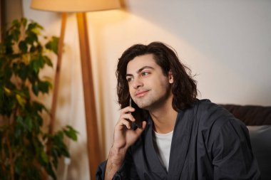 İyi görünümlü genç bir adam evde rahat bir şekilde giyinip telefonla konuşuyor..