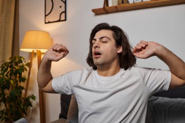 A young man stretches contentedly at home in his stylish apartment, enjoying a moment of leisure. clipart