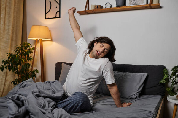 Young man stretches in bed, embracing the peaceful morning light of his home.