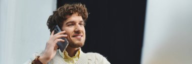 Modern ofis ortamında otururken telefonda kıvırcık saçlı genç bir profesyonel konuşuyor.