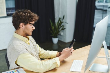 Young man in corporate attire focuses on smartphone while working at a sleek office desk. clipart