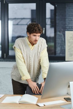 Genç kıvırcık saçlı bir adam hafta içi şık bir ofis masasında işine odaklanır..