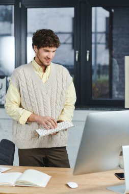 Kıvırcık saçlı bir genç, modaya uygun bir ofis ortamındaki bir bilgisayara odaklanmış durumda..