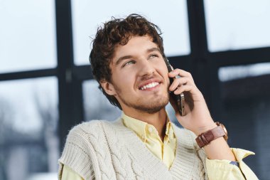 Modern ofis ortamında oturan kıvırcık saçlı genç bir adam telefonda konuşuyor..