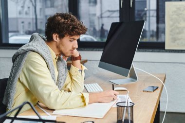 Gri kazaklı genç adam şık bir ofis masasında işine odaklanıyor..