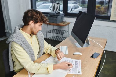 Curly-haired young man focuses on his work while seated at a stylish desk in a contemporary office. clipart