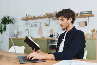 Şık bir dairede, yakışıklı genç bir adam laptopuyla çalışırken düşünceli bir şekilde okur..