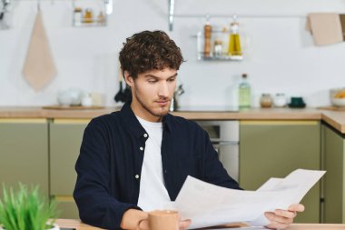 Young man sits comfortably in his stylish apartment, focused on reading important papers. clipart