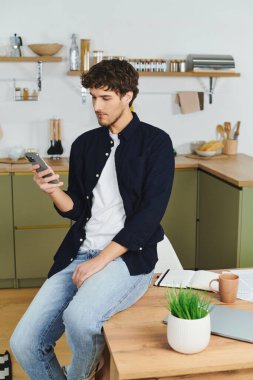 Yakışıklı genç bir adam şık bir dairede rahat bir şekilde oturuyor, telefonuyla kayıyor..