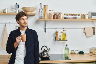 Kıvırcık saçlı adam kahvesini yudumluyor, çağdaş dairesinde huzurun tadını çıkarıyor..