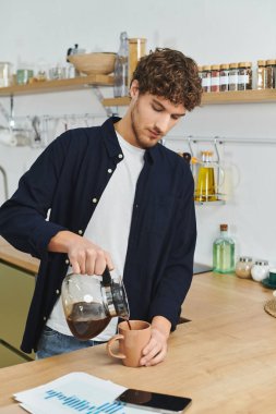 Curly-haired man prepares his morning coffee in a sleek apartment setting, radiating calmness. clipart