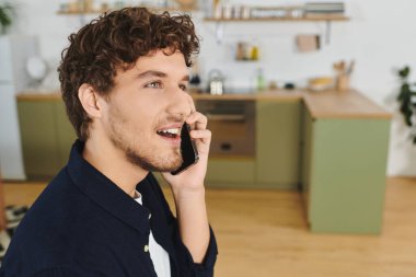 Yakışıklı genç adam şık dairesinde dinlenirken telefonla konuşuyor, gülümsüyor..