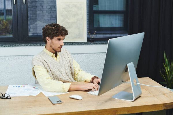 Волосатый мужчина в свитере фокусируется на компьютерных задачах в современной офисной обстановке