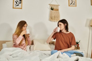 İki genç, modaya uygun tasarlanmış bir yatak odasında sohbet ederken sıcak içeceklerden hoşlanırlar..