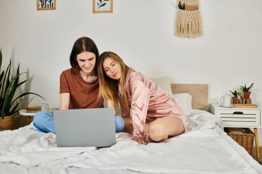 Two young individuals share a warm connection as they explore a laptop together in a chic space. clipart