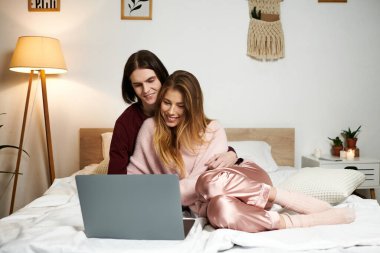 A young couple sits together on their bed, engaged in a warm and collaborative activity. clipart