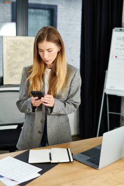 Modern ofis elemanlarıyla çevriliyken, odaklanmış genç bireyler akıllı telefon ile etkileşime giriyor..