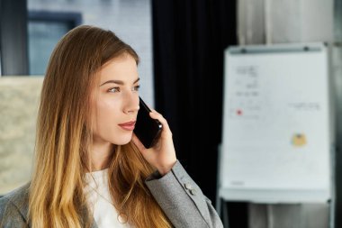 Genç ve şık bir kadın şık bir ofiste iş saatlerinde akıllı telefonuyla konuşur..