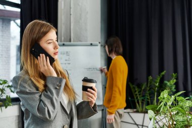 Genç bir birey modern bir çalışma alanında iş arkadaşının yanında telefonla konuşmaktan zevk alır..