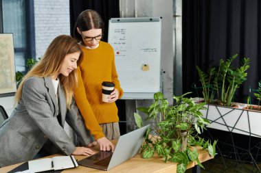 İki genç insan, yeni bitkilerle çevrili modern bir ofiste iş birliği yapıyor..