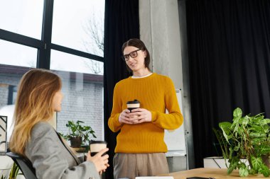 Two young individuals share ideas while enjoying coffee in a stylish office environment. clipart