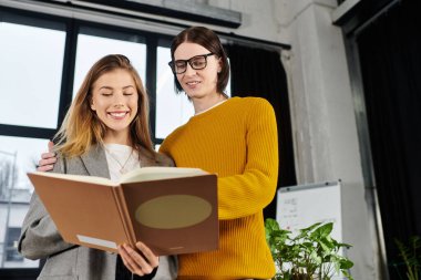 Cheerful young individuals share a special moment while reading together in a modern location. clipart