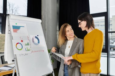 Gündüz vakti çağdaş bir çalışma alanında genç bireyler renkli çizelgeler üzerinde sohbet ediyorlar..