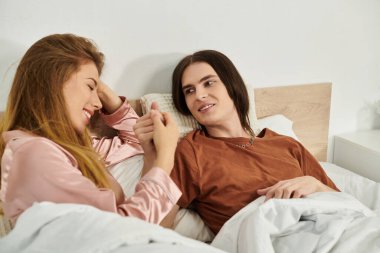 İki genç insan birlikte yatakta dinlenirken gülüp eğleniyorlar..