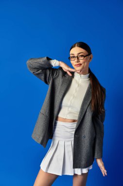 Genç bir kadın, kendine güvenen bir gülümseme ve neşeli bir pozla moda anlayışını sergiliyor..