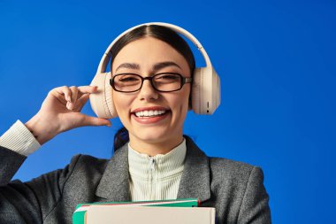 Gözlüklü güzel bir kadın, müzik dinlerken ve elinde kitaplarla gülümsüyor..