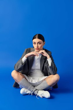 Düşünceli bir ifadeye sahip genç bir kadın bacak bacak üstüne atmış, derin duygular ve stil aktarıyor..