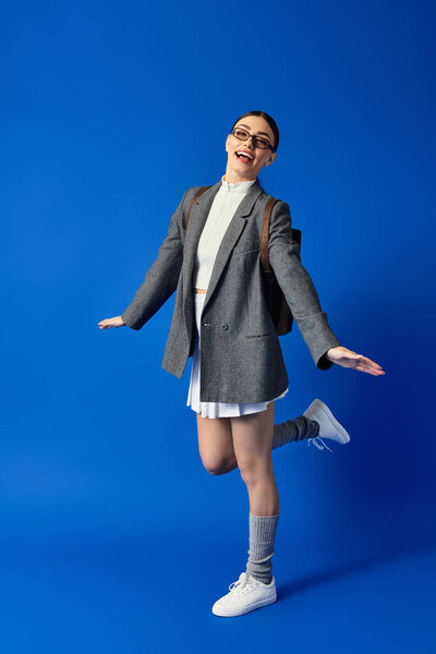 Молодая женщина в очках игриво позирует в стильном наряде, демонстрируя свое волнение.