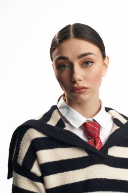 Güzel genç bir kadın, şık çizgili bir süveter ve kırmızı bir kravat takmış, düşünceli bir şekilde bakıyor..