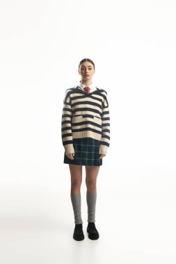 Genç bir kadın, modaya uygun çizgili bir kazak ve etek giyerken derin duygular ifade eder..