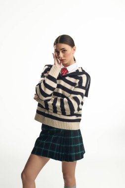 Düşünceli bir görünüşü olan genç bir kadın basit bir arkaplana karşı duruyor ve tarzını gösteriyor..