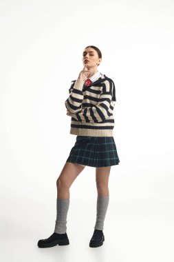 Güzel bir kadın kendine güvenerek ayakta duruyor, yansıtıcı bir ifadeyle modaya uygun bir kıyafet giyiyor..