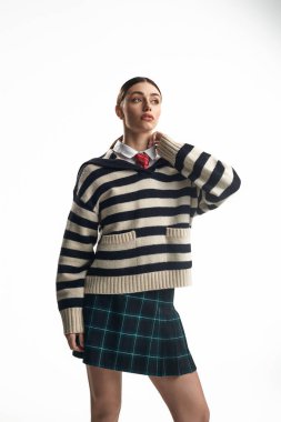 Canlı bir stüdyoda, genç bir kadın çizgili süveter ve ekose etekle duygularını sergiliyor..