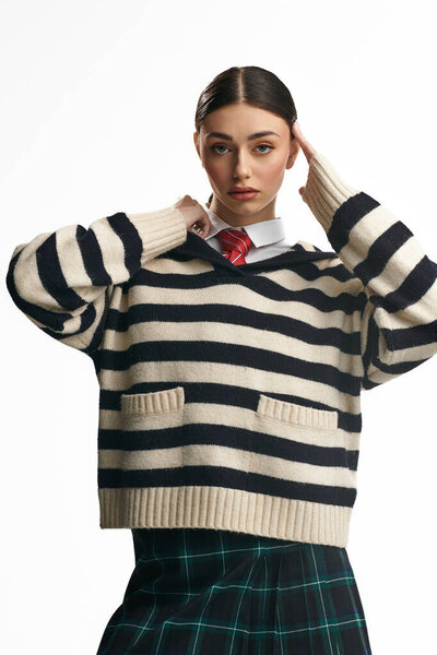 Красивая молодая женщина выражает свои эмоции в стильном полосатом свитере и клетчатой юбке.