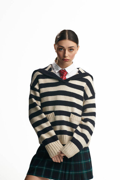 Молодая женщина демонстрирует вдумчивое выражение лица, одетая в стильный полосатый свитер и юбку.