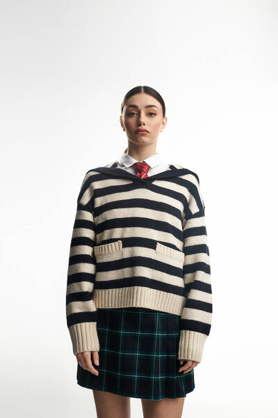 Красивая молодая женщина эмоционально увлечена, одета в полосатый свитер и клетчатую юбку.