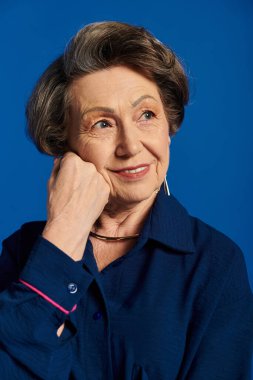 60 'lı yaşlarındaki güzel bir kadın kendine güvenerek şık bir şekilde poz verir, zarafet ve cazibe saçar..