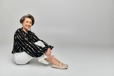 Şık giyinmiş olgun bir kadın zarifçe poz verirken zarafet ve güven yayar..