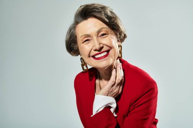 60 'lı yaşlardaki güzel bir kadın kendine güvenerek şık bir şekilde poz verir, zarafet ve cazibe saçar..