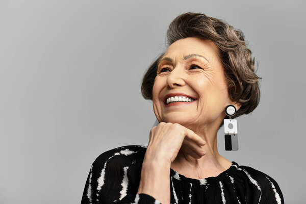 A confident and stylish woman in her 60s showcases elegance against a grey backdrop.