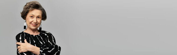 A beautiful woman in her 60s poses gracefully, showcasing her elegant style against a grey backdrop, banner