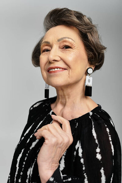 Красивая женщина в ее 60-х позирует грациозно, носить элегантный наряд и источать вневременной стиль.